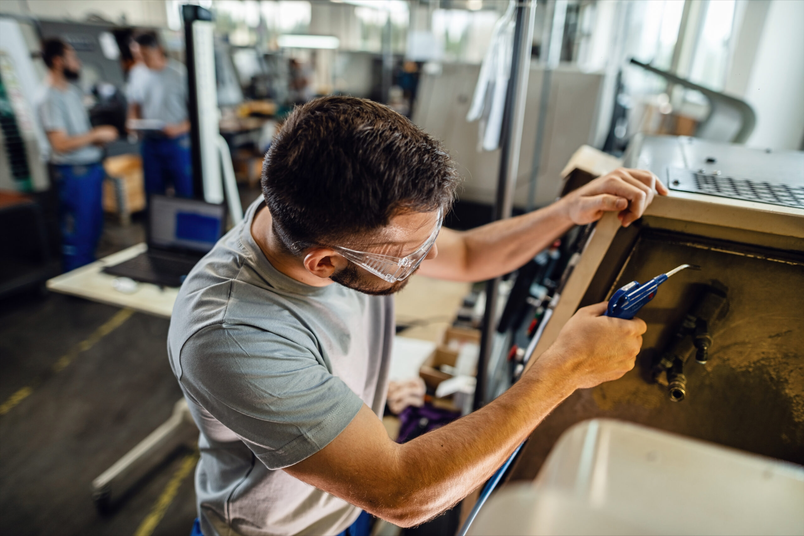 Young manual worker working at industrial machine in a factory plant.